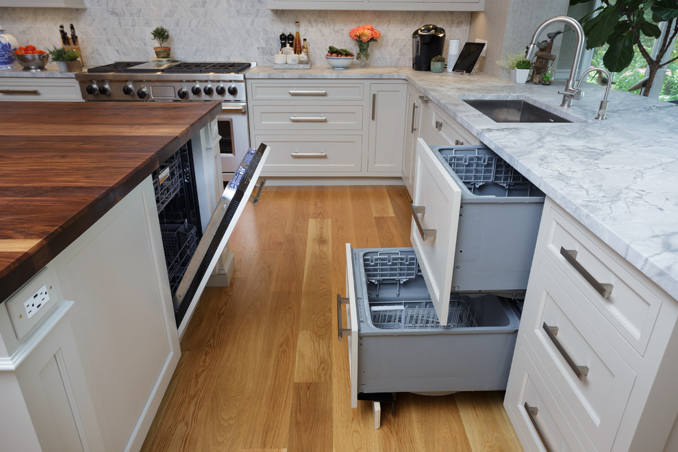 Example of a large classic u-shaped light wood floor and beige floor enclosed kitchen design in Philadelphia with an undermount sink, recessed-panel cabinets, white cabinets, marble countertops, white backsplash, marble backsplash, paneled appliances and two islands