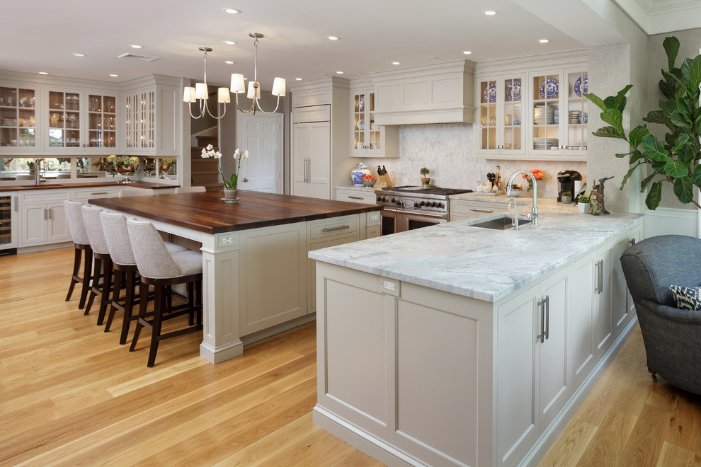 Inspiration for a large timeless u-shaped light wood floor and beige floor enclosed kitchen remodel in Philadelphia with an undermount sink, recessed-panel cabinets, white cabinets, marble countertops, white backsplash, marble backsplash, paneled appliances and two islands