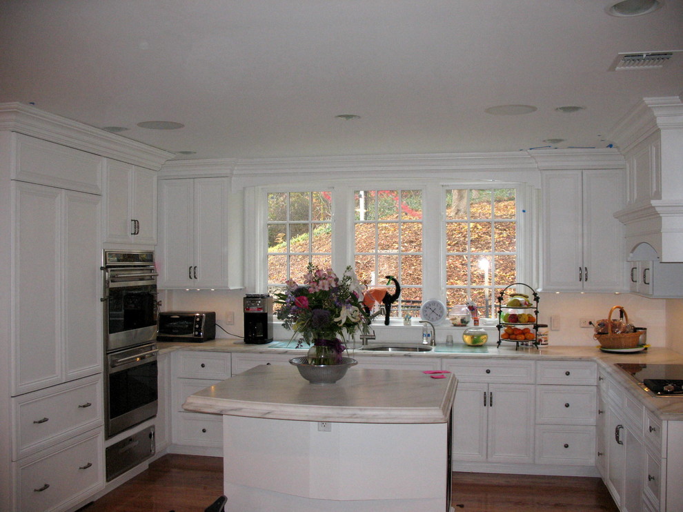 Immagine di una cucina tradizionale con lavello sottopiano, ante con riquadro incassato, ante bianche, paraspruzzi bianco, elettrodomestici in acciaio inossidabile, pavimento in legno massello medio e top in marmo