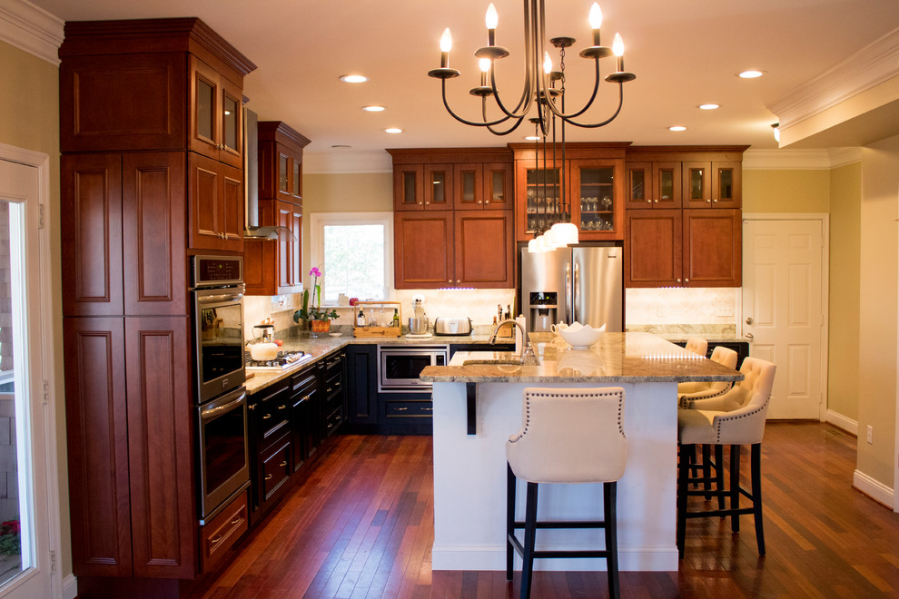 Inspiration for a large transitional l-shaped dark wood floor and brown floor enclosed kitchen remodel in DC Metro with a double-bowl sink, raised-panel cabinets, dark wood cabinets, granite countertops, beige backsplash, limestone backsplash, stainless steel appliances and an island