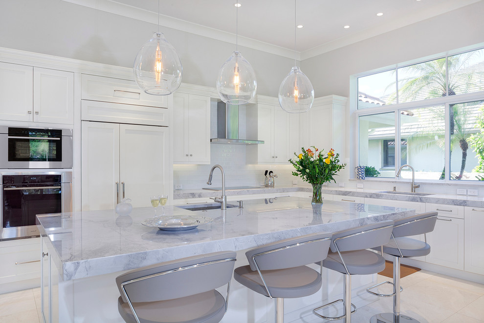 Example of a large transitional galley marble floor and white floor eat-in kitchen design in Miami with a drop-in sink, recessed-panel cabinets, white cabinets, marble countertops, white backsplash, glass tile backsplash, stainless steel appliances, an island and gray countertops