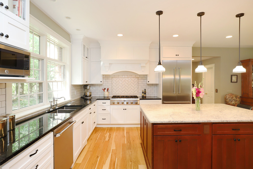 Photo of a medium sized traditional u-shaped kitchen/diner in Grand Rapids with a double-bowl sink, shaker cabinets, white cabinets, engineered stone countertops, white splashback, metro tiled splashback, stainless steel appliances, light hardwood flooring, an island and brown floors.