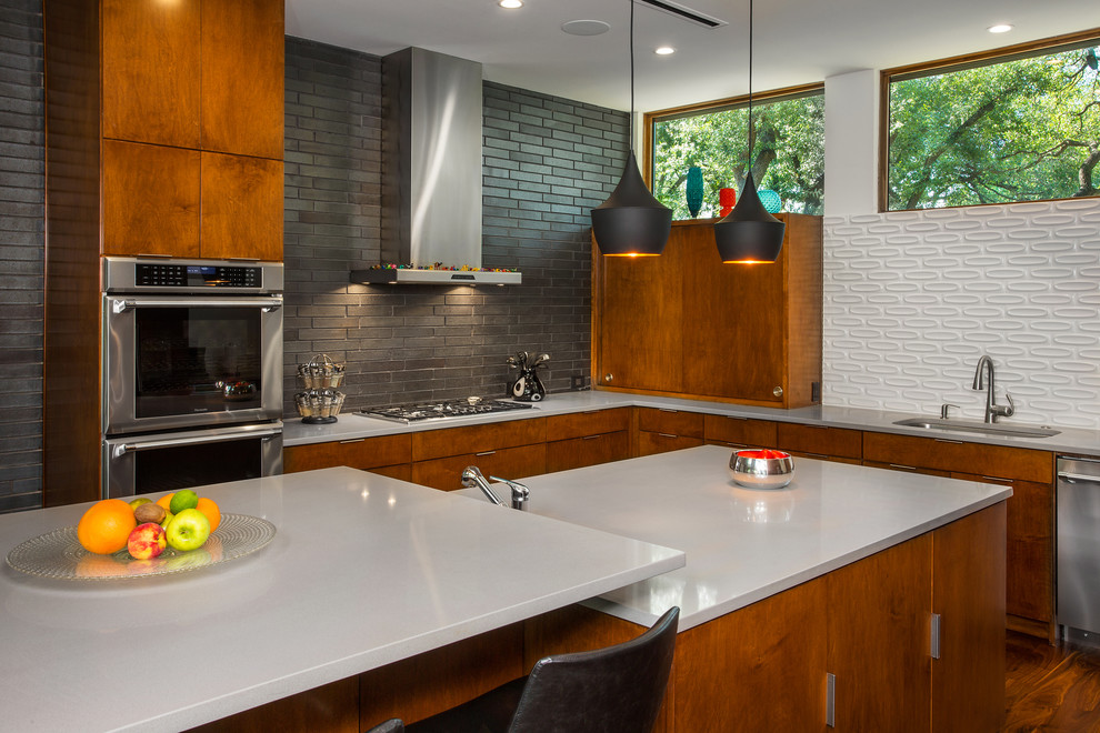 This is an example of a medium sized midcentury u-shaped open plan kitchen in Dallas with a submerged sink, flat-panel cabinets, medium wood cabinets, engineered stone countertops, white splashback, ceramic splashback, stainless steel appliances, medium hardwood flooring, multiple islands, brown floors and white worktops.