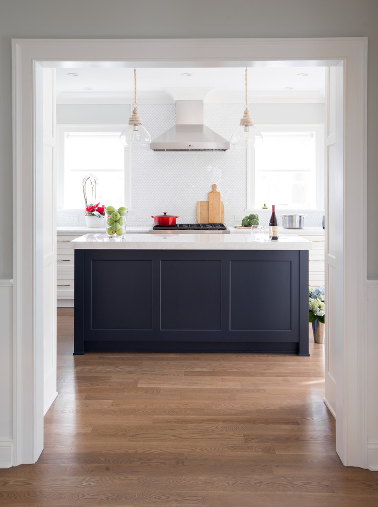 Exemple d'une cuisine américaine chic de taille moyenne avec un évier encastré, un placard à porte shaker, des portes de placard blanches, plan de travail en marbre, une crédence blanche, une crédence en carrelage de pierre, un électroménager en acier inoxydable, un sol en bois brun et îlot.