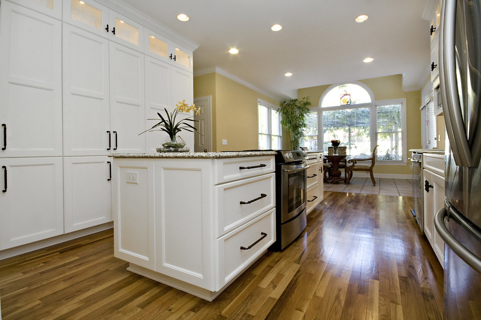 Mid-sized transitional galley medium tone wood floor and orange floor eat-in kitchen photo in Raleigh with an undermount sink, recessed-panel cabinets, white cabinets, granite countertops, multicolored backsplash, stainless steel appliances, glass tile backsplash, an island and multicolored countertops