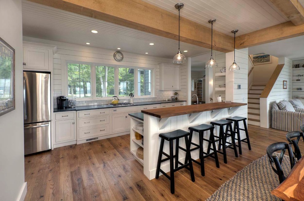 Photo of a medium sized nautical galley open plan kitchen in Other with beaded cabinets, white cabinets, white splashback, stainless steel appliances, a breakfast bar, metro tiled splashback and dark hardwood flooring.