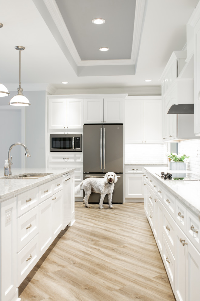 Klassisk inredning av ett mycket stort flerfärgad flerfärgat kök, med en trippel diskho, skåp i shakerstil, vita skåp, bänkskiva i kvarts, vitt stänkskydd, stänkskydd i marmor, rostfria vitvaror, ljust trägolv, en köksö och grått golv
