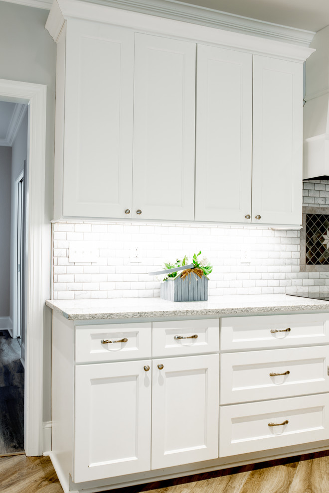 Inredning av ett klassiskt mycket stort flerfärgad flerfärgat kök, med en trippel diskho, skåp i shakerstil, vita skåp, bänkskiva i kvarts, vitt stänkskydd, stänkskydd i marmor, rostfria vitvaror, ljust trägolv, en köksö och grått golv