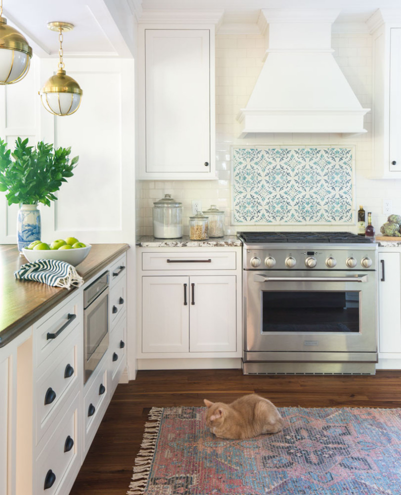 Exempel på ett avskilt, mellanstort klassiskt beige beige u-kök, med en rustik diskho, släta luckor, vita skåp, granitbänkskiva, blått stänkskydd, stänkskydd i keramik, rostfria vitvaror, mellanmörkt trägolv, en halv köksö och brunt golv