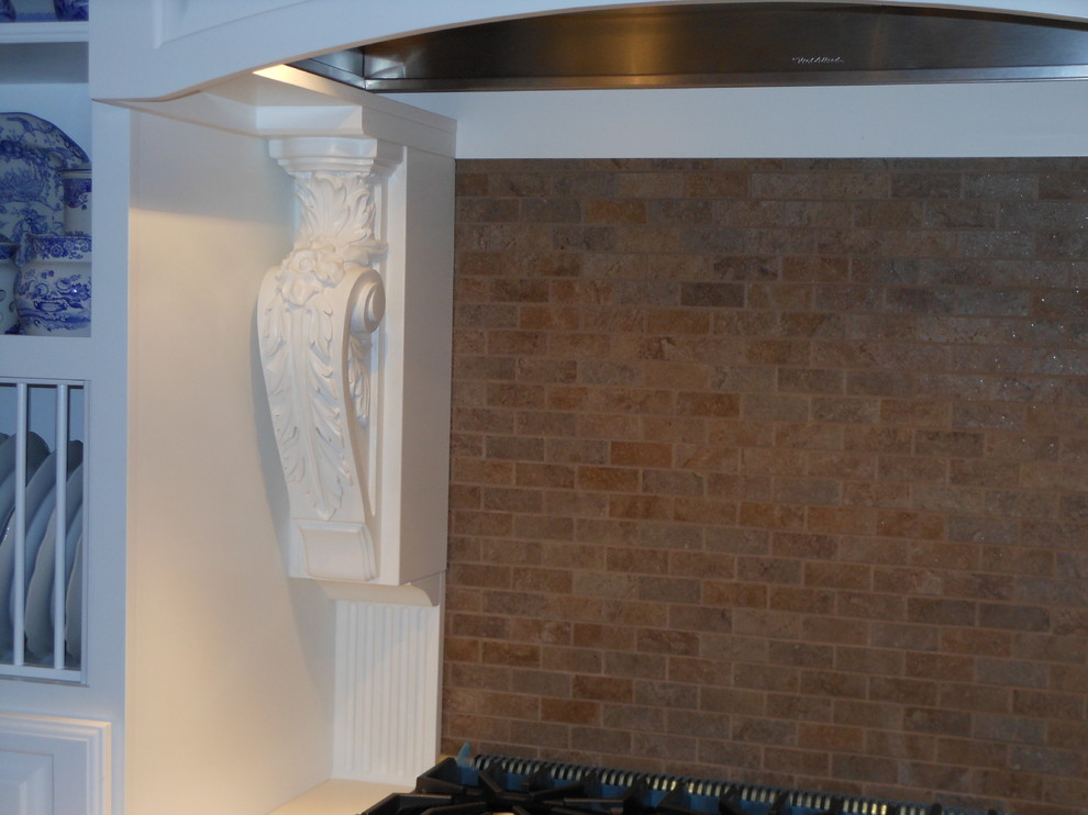 Klassisk inredning av ett kök, med en nedsänkt diskho, vita skåp, bänkskiva i koppar, brunt stänkskydd, stänkskydd i stenkakel och vita vitvaror