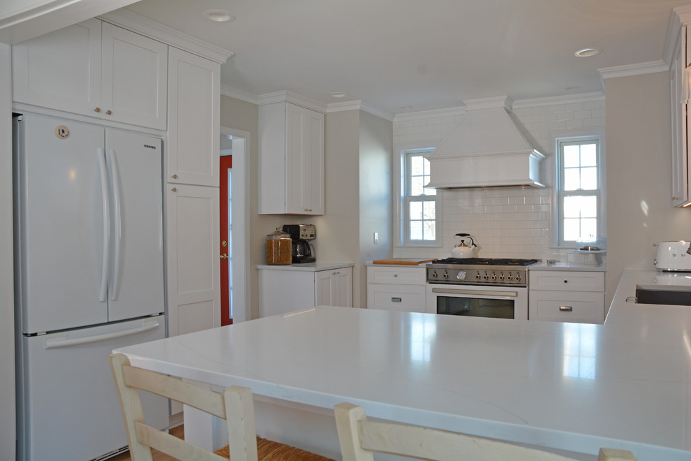 Foto på ett mellanstort vintage vit kök, med en undermonterad diskho, skåp i shakerstil, vita skåp, bänkskiva i kvarts, vitt stänkskydd, stänkskydd i keramik, vita vitvaror, ljust trägolv, en halv köksö och brunt golv