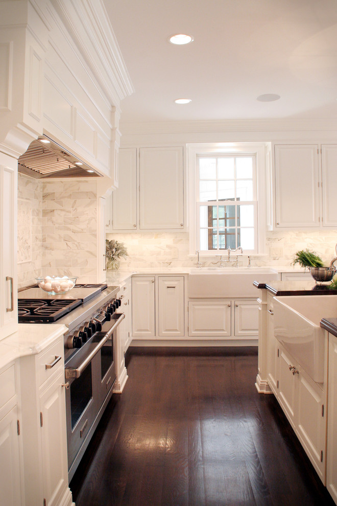 Elegant kitchen photo in Cleveland with stainless steel appliances, a farmhouse sink, white backsplash, raised-panel cabinets, white cabinets and marble backsplash