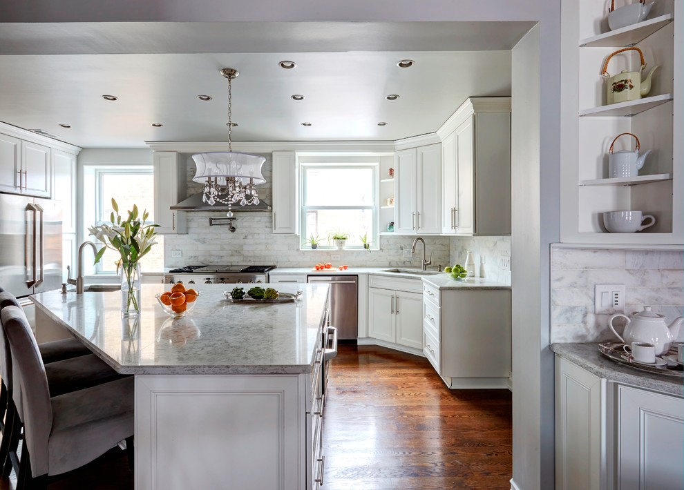 This is an example of a large bohemian l-shaped kitchen/diner in Chicago with a single-bowl sink, recessed-panel cabinets, white cabinets, engineered stone countertops, white splashback, marble splashback, stainless steel appliances, dark hardwood flooring, an island and brown floors.