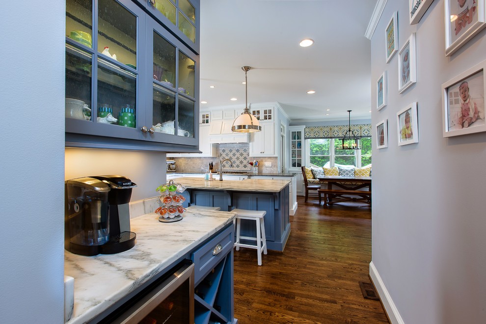 Eat-in kitchen - large transitional l-shaped medium tone wood floor eat-in kitchen idea in Atlanta with a farmhouse sink, shaker cabinets, white cabinets, soapstone countertops, white backsplash, stone tile backsplash, stainless steel appliances and an island