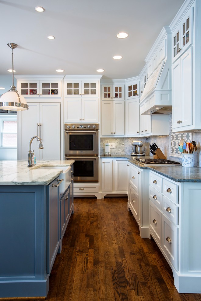 This is an example of a large traditional l-shaped kitchen/diner in Atlanta with a belfast sink, shaker cabinets, white cabinets, soapstone worktops, white splashback, stone tiled splashback, stainless steel appliances, medium hardwood flooring and an island.