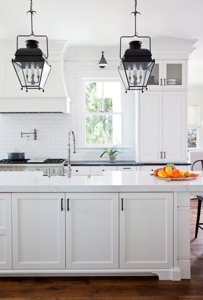 Exempel på ett klassiskt flerfärgad flerfärgat kök, med en rustik diskho, skåp i shakerstil, vita skåp, granitbänkskiva, vitt stänkskydd, stänkskydd i keramik, vita vitvaror, ljust trägolv, en köksö och brunt golv