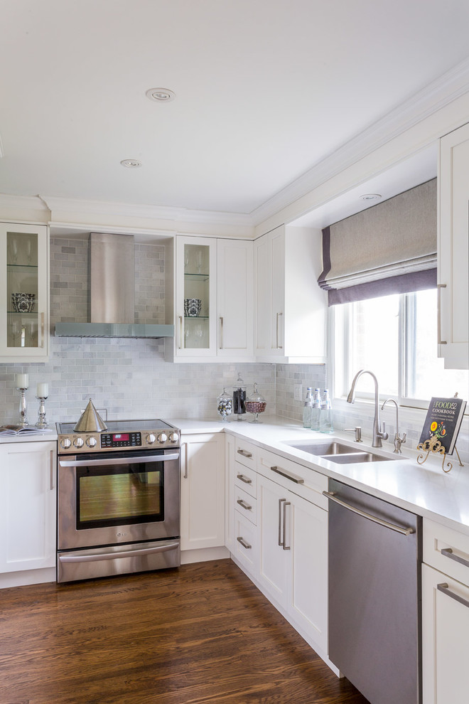Inspiration for a small transitional u-shaped dark wood floor kitchen remodel in Toronto with an undermount sink, shaker cabinets, white cabinets, quartzite countertops, white backsplash, stone tile backsplash, stainless steel appliances and a peninsula