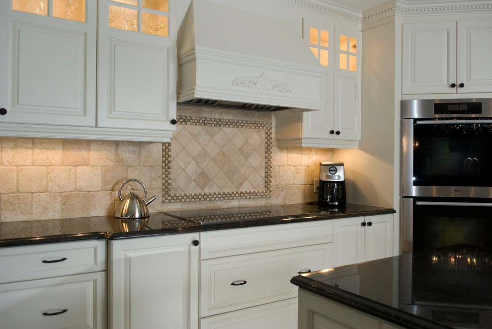 Exempel på ett stort klassiskt brun brunt kök, med en undermonterad diskho, luckor med upphöjd panel, vita skåp, granitbänkskiva, beige stänkskydd, stänkskydd i travertin, rostfria vitvaror, klinkergolv i keramik, en köksö och brunt golv