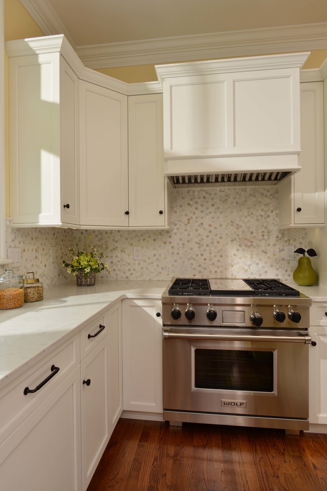 Foto på ett mellanstort vintage vit l-kök, med släta luckor, vita skåp, bänkskiva i kvarts, stänkskydd i marmor, rostfria vitvaror, mellanmörkt trägolv och en köksö