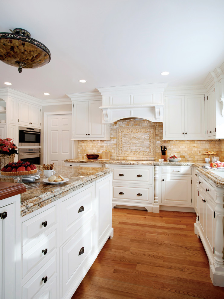 Große Klassische Wohnküche in U-Form mit profilierten Schrankfronten, weißen Schränken, Granit-Arbeitsplatte, Küchengeräten aus Edelstahl, hellem Holzboden und Kücheninsel in Sonstige