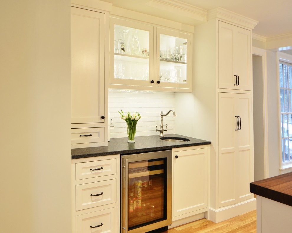 ボストンにある広いトラディショナルスタイルのおしゃれなキッチン (エプロンフロントシンク、フラットパネル扉のキャビネット、白いキャビネット、御影石カウンター、白いキッチンパネル、セラミックタイルのキッチンパネル、シルバーの調理設備、淡色無垢フローリング) の写真