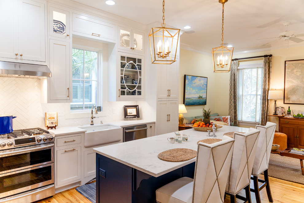 Example of a large transitional l-shaped medium tone wood floor open concept kitchen design in Charleston with a farmhouse sink, white cabinets, quartz countertops, white backsplash, stainless steel appliances, an island and recessed-panel cabinets