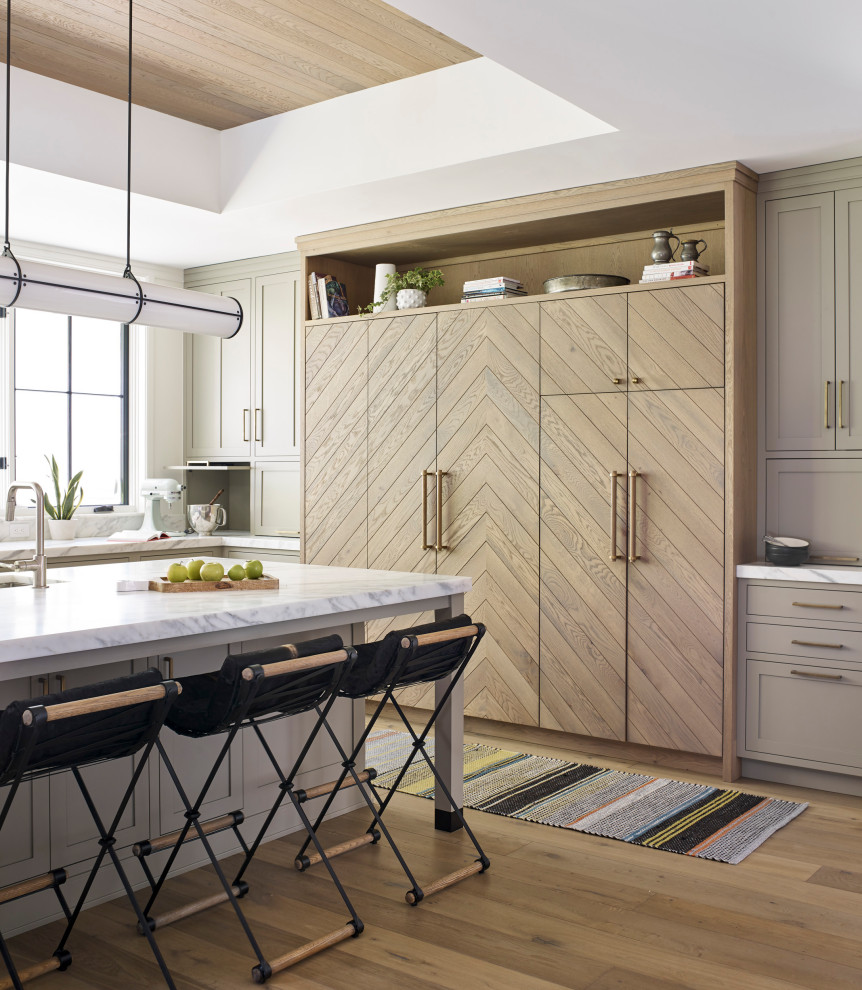 Example of a large transitional l-shaped medium tone wood floor and brown floor open concept kitchen design in New York with an undermount sink, light wood cabinets, marble countertops, white backsplash, marble backsplash, an island, white countertops, flat-panel cabinets and paneled appliances