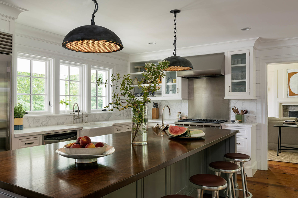 Bild på ett lantligt l-kök, med en rustik diskho, skåp i shakerstil, vita skåp, träbänkskiva, vitt stänkskydd, stänkskydd i sten, rostfria vitvaror, mellanmörkt trägolv, en köksö och brunt golv