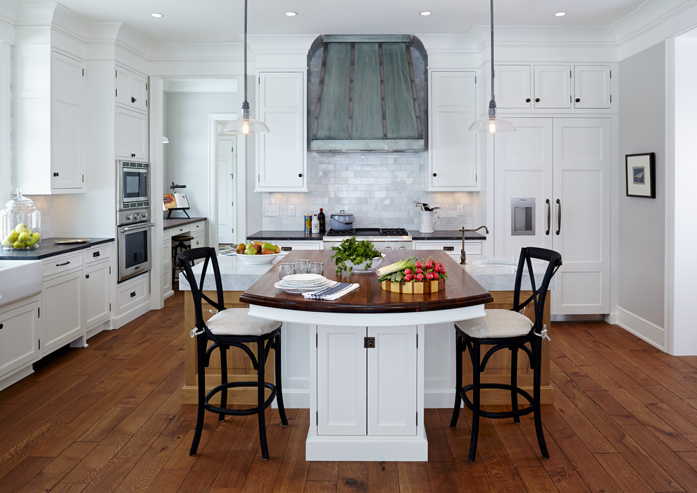 Beach style l-shaped dark wood floor kitchen photo in Minneapolis with a farmhouse sink, shaker cabinets, white cabinets, wood countertops, white backsplash, paneled appliances and marble backsplash
