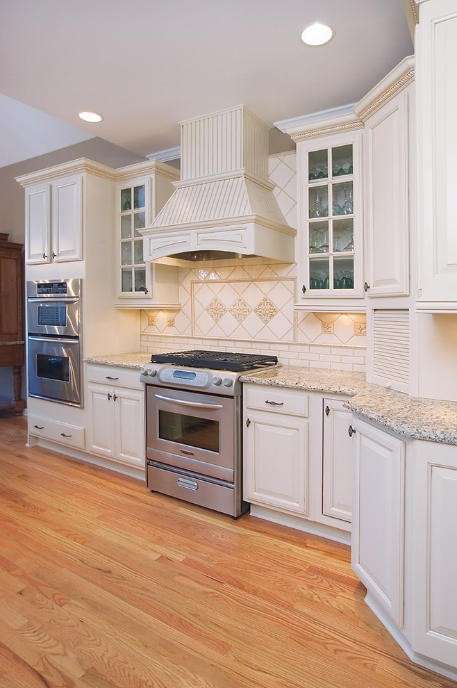 Exempel på ett mellanstort modernt kök, med en undermonterad diskho, luckor med upphöjd panel, vita skåp, granitbänkskiva, beige stänkskydd, stänkskydd i porslinskakel, rostfria vitvaror, ljust trägolv och en köksö