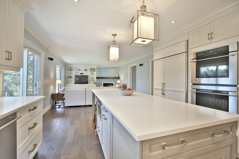 This is an example of a large traditional open plan kitchen in Toronto with a submerged sink, shaker cabinets, white cabinets, quartz worktops, white splashback, dark hardwood flooring and an island.