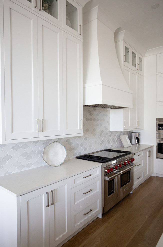 Inredning av ett klassiskt stort vit vitt kök, med en rustik diskho, skåp i shakerstil, vita skåp, bänkskiva i kvartsit, vitt stänkskydd, stänkskydd i keramik, rostfria vitvaror, mellanmörkt trägolv, en köksö och beiget golv