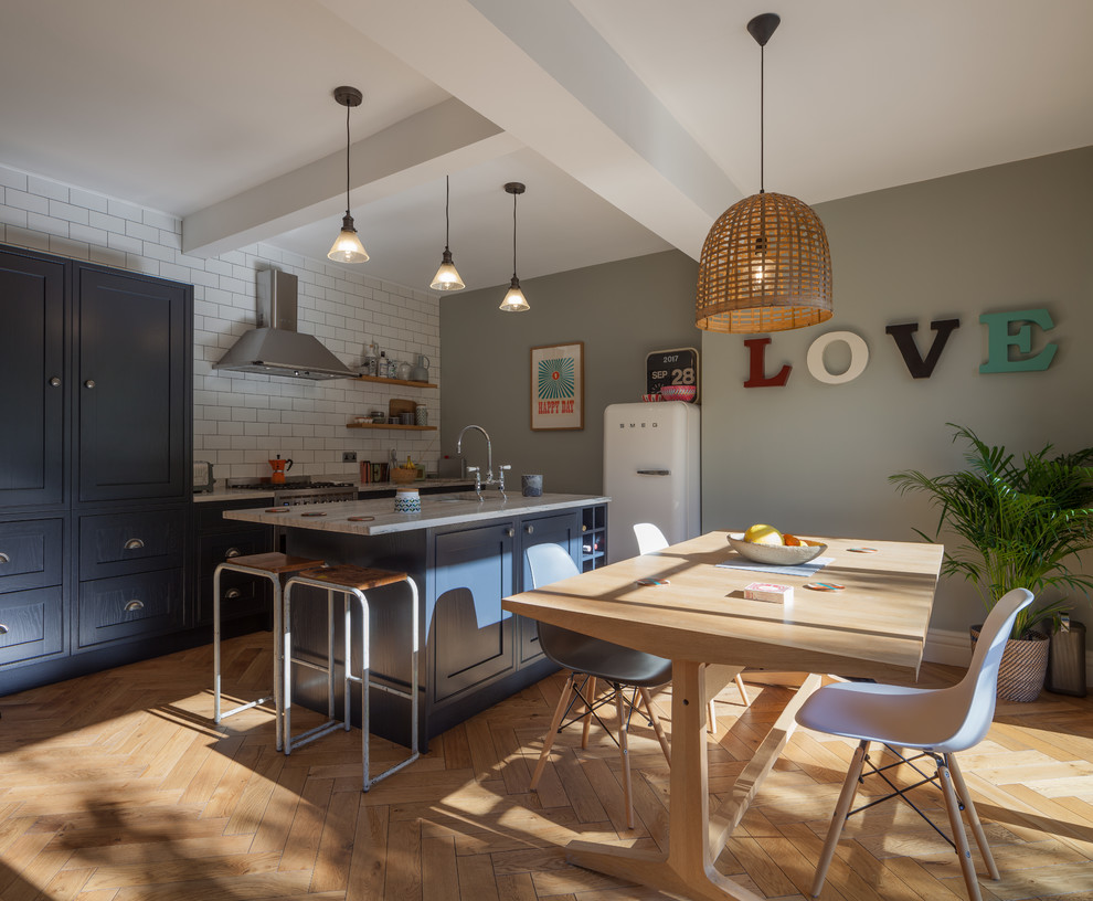 This is an example of a contemporary galley kitchen/diner in Manchester with a built-in sink, shaker cabinets, grey cabinets, white splashback, ceramic splashback, light hardwood flooring and an island.