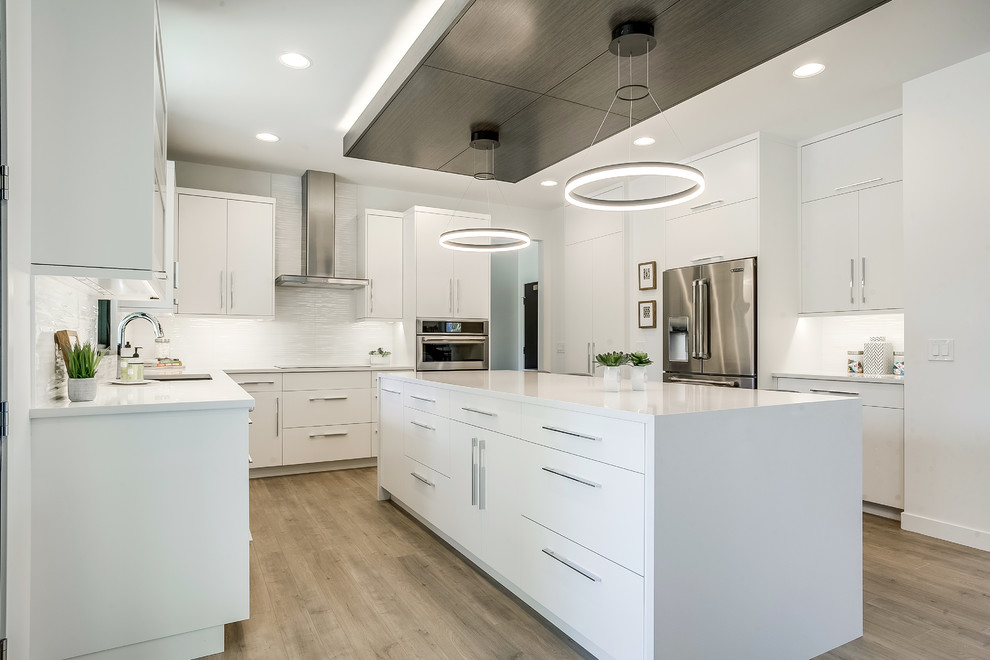 Moderne Küche in U-Form mit Unterbauwaschbecken, flächenbündigen Schrankfronten, weißen Schränken, braunem Holzboden, Kücheninsel, braunem Boden und weißer Arbeitsplatte in Grand Rapids