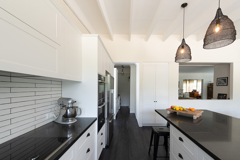 Foto på ett stort lantligt svart kök, med en undermonterad diskho, skåp i shakerstil, vita skåp, bänkskiva i kvarts, vitt stänkskydd, stänkskydd i keramik, laminatgolv, en köksö och svart golv