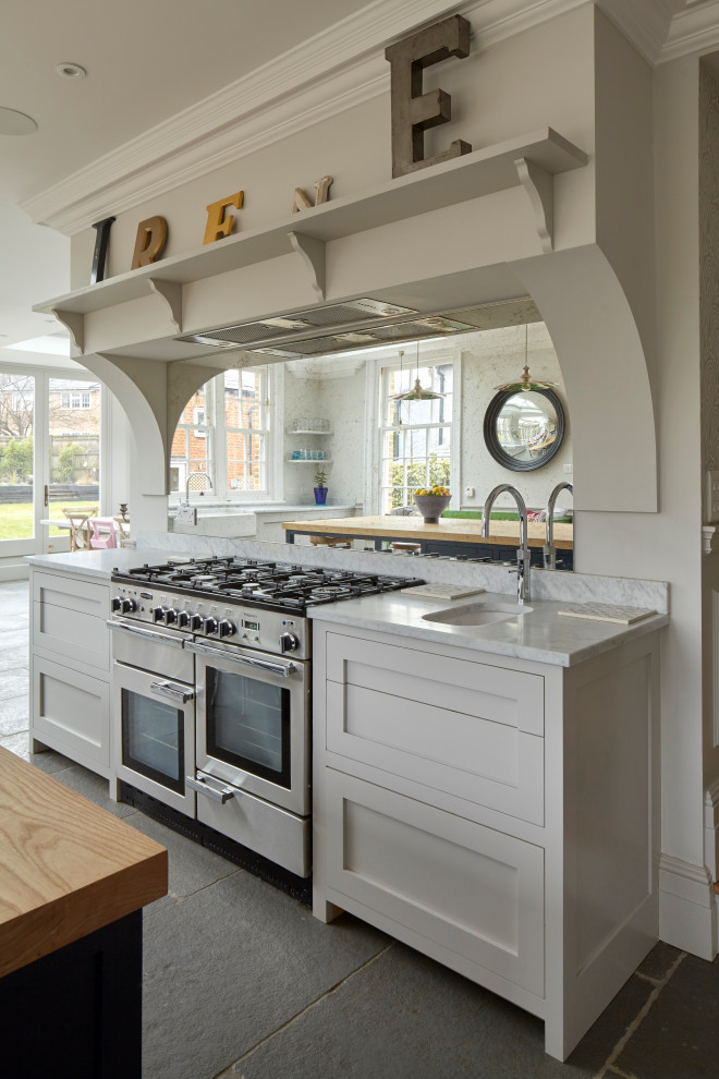 Photo of a large contemporary open plan kitchen in Surrey with a belfast sink, shaker cabinets, grey cabinets, marble worktops, mirror splashback, stainless steel appliances, limestone flooring, an island, grey floors and white worktops.