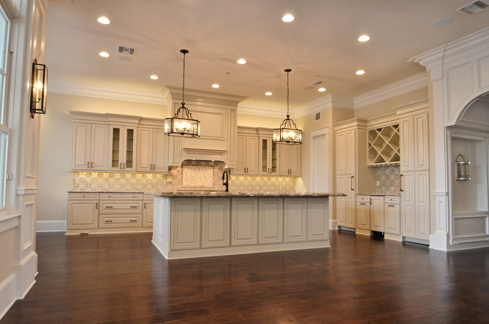 Open concept kitchen - mid-sized traditional l-shaped dark wood floor open concept kitchen idea in New Orleans with an undermount sink, raised-panel cabinets, white cabinets, granite countertops, beige backsplash, stainless steel appliances and an island
