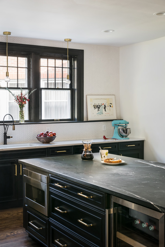 Photo of a classic l-shaped kitchen/diner in St Louis with a single-bowl sink, raised-panel cabinets, black cabinets, soapstone worktops, white splashback, ceramic splashback, stainless steel appliances, medium hardwood flooring, an island, brown floors and black worktops.