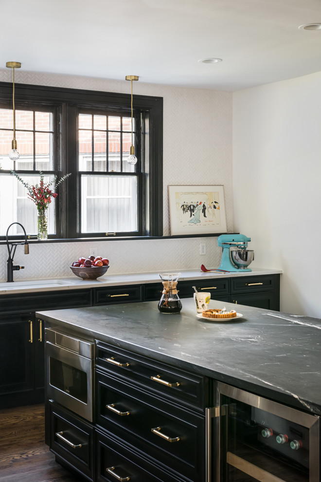 Bild på ett stort vintage grå grått kök och matrum, med luckor med upphöjd panel, svarta skåp, bänkskiva i täljsten, vitt stänkskydd, stänkskydd i keramik, rostfria vitvaror, mellanmörkt trägolv, en köksö och brunt golv