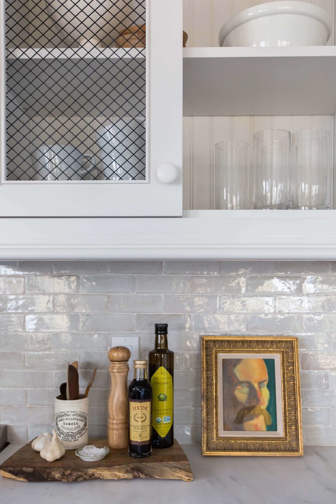 Bild på ett litet vintage kök, med vita skåp, marmorbänkskiva, vitt stänkskydd, stänkskydd i terrakottakakel, rostfria vitvaror, mellanmörkt trägolv, en köksö och luckor med infälld panel