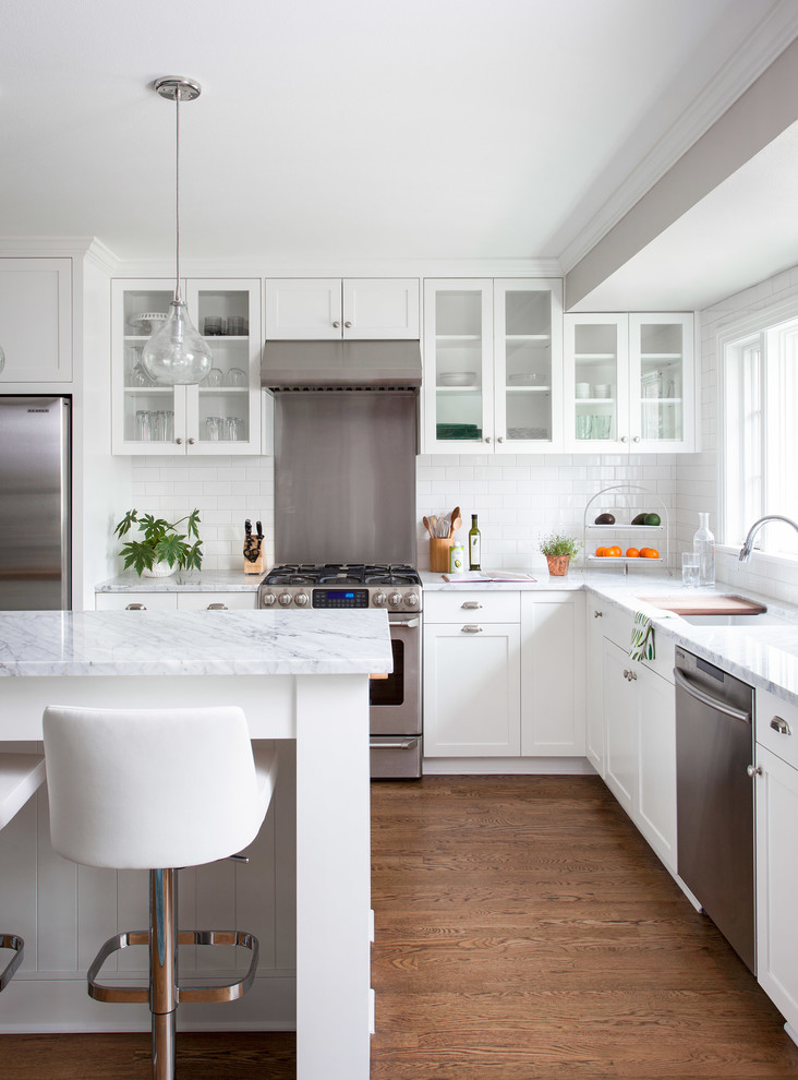 Foto på ett mellanstort vintage l-kök, med en undermonterad diskho, luckor med glaspanel, vita skåp, marmorbänkskiva, vitt stänkskydd, stänkskydd i tunnelbanekakel, rostfria vitvaror, mörkt trägolv och en köksö