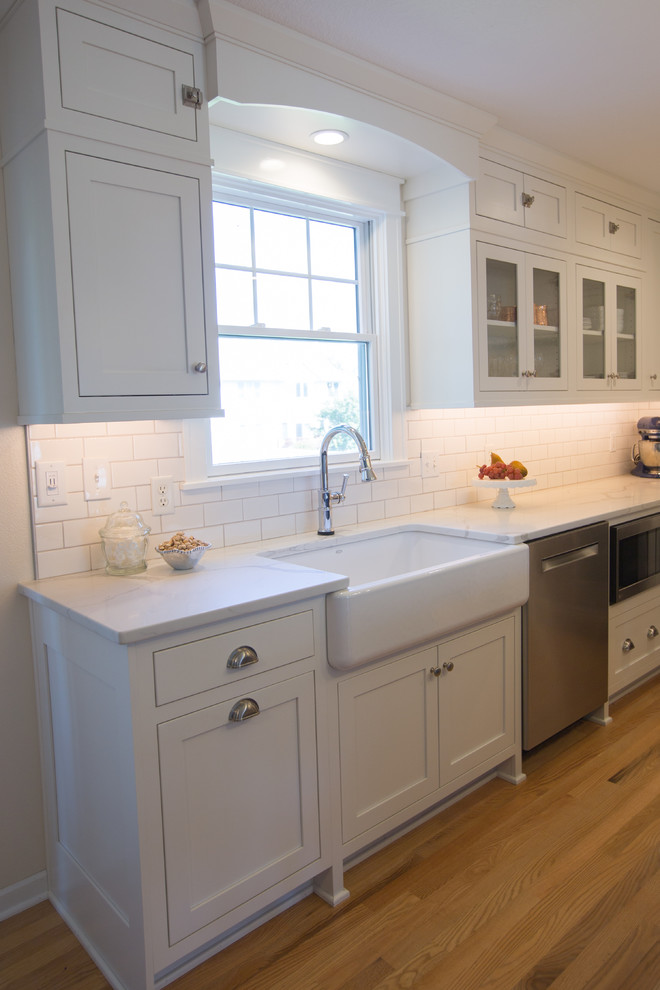 Inredning av ett lantligt litet kök, med en rustik diskho, skåp i shakerstil, blå skåp, bänkskiva i kvarts, vitt stänkskydd, stänkskydd i porslinskakel, rostfria vitvaror, ljust trägolv, en köksö och brunt golv