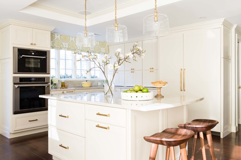 This is an example of a classic l-shaped kitchen in Boston with recessed-panel cabinets, beige cabinets, integrated appliances, dark hardwood flooring, an island and brown floors.