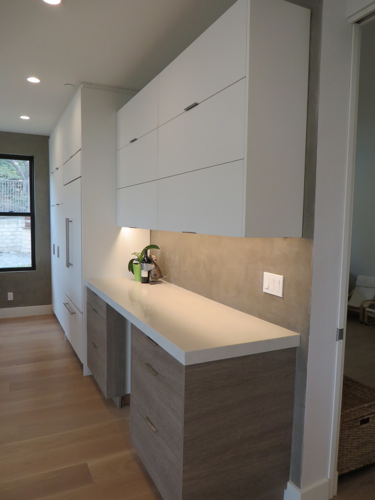 Large contemporary l-shaped kitchen/diner in Orange County with flat-panel cabinets, grey splashback, integrated appliances, light hardwood flooring, an island, a single-bowl sink, medium wood cabinets, engineered stone countertops and white worktops.