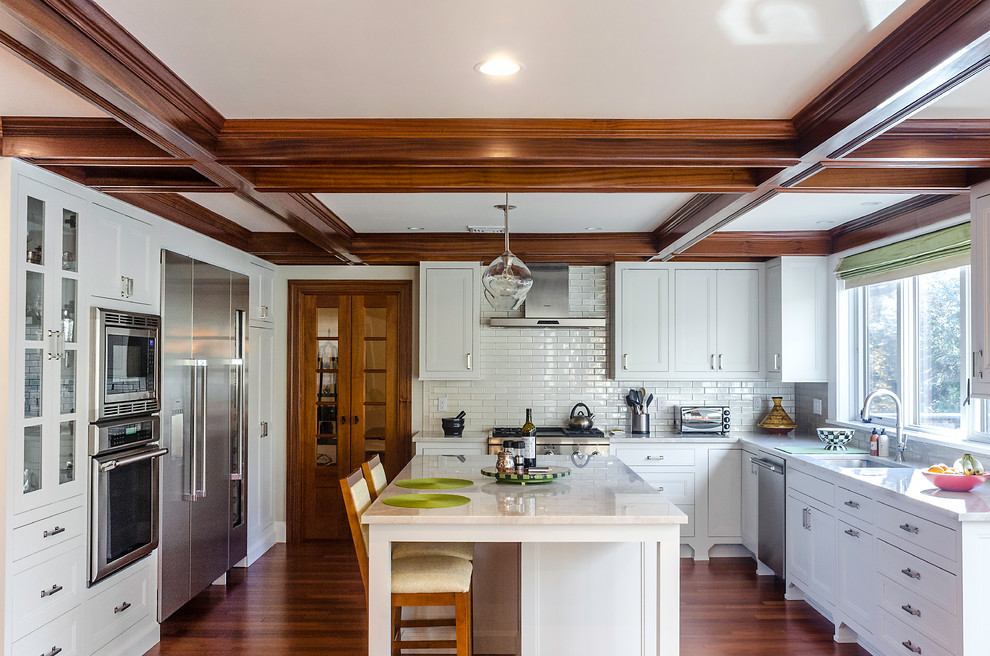 Example of a mid-sized transitional u-shaped medium tone wood floor open concept kitchen design in New York with an undermount sink, shaker cabinets, white cabinets, granite countertops, white backsplash, subway tile backsplash, stainless steel appliances and an island