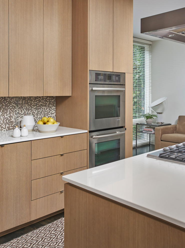 Идея дизайна: кухня-гостиная в стиле модернизм с плоскими фасадами, коричневым фартуком, техникой из нержавеющей стали, островом и белой столешницей