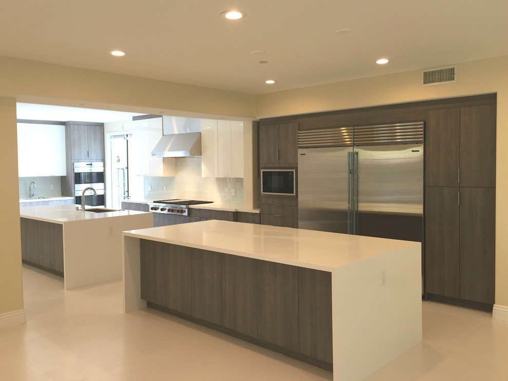 Large modern galley kitchen/diner in Orange County with a submerged sink, flat-panel cabinets, medium wood cabinets, engineered stone countertops, white splashback, glass tiled splashback, stainless steel appliances, porcelain flooring and multiple islands.