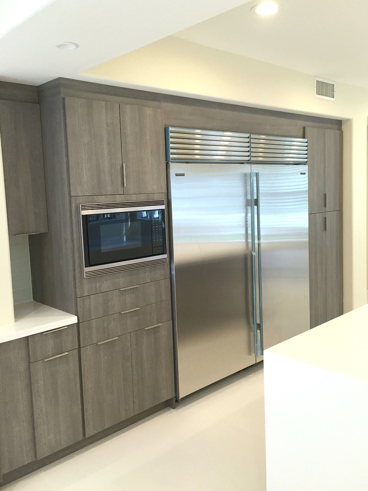 This is an example of a large modern galley kitchen/diner in Orange County with a submerged sink, flat-panel cabinets, medium wood cabinets, engineered stone countertops, white splashback, glass tiled splashback, stainless steel appliances, porcelain flooring and multiple islands.