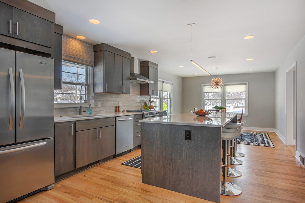 Example of a mid-sized trendy galley light wood floor eat-in kitchen design in Grand Rapids with an undermount sink, flat-panel cabinets, gray cabinets, quartz countertops, gray backsplash, ceramic backsplash and stainless steel appliances