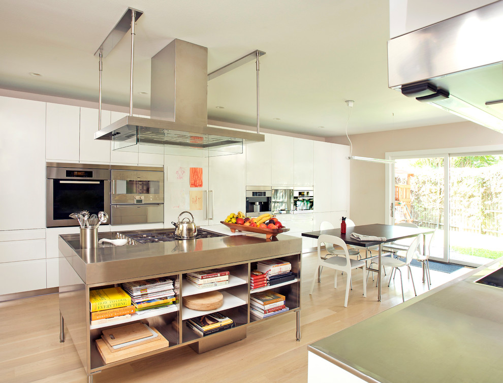Foto di una cucina design con ante lisce, ante bianche, elettrodomestici in acciaio inossidabile e parquet chiaro